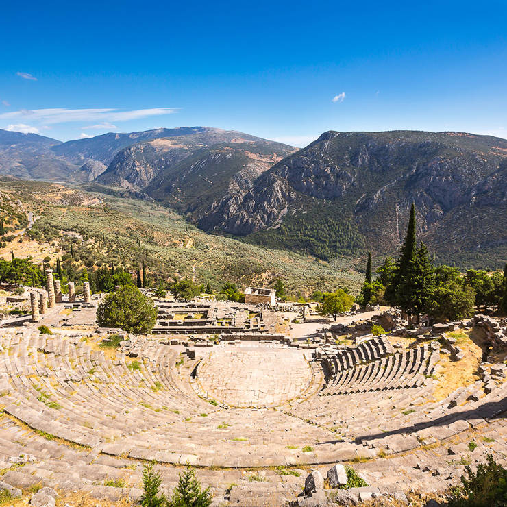 Ancient theater of Delphi surrounded by greenery and mountains under a bright sky