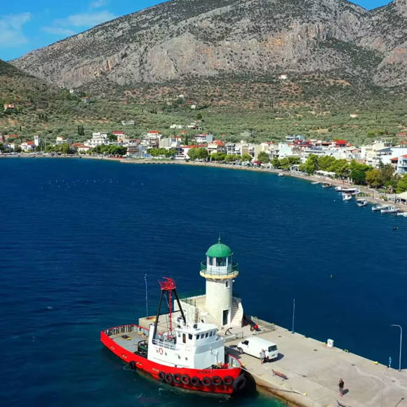 Aerial view of Antikira lighthouse with the seaside village and mountains in the backdrop