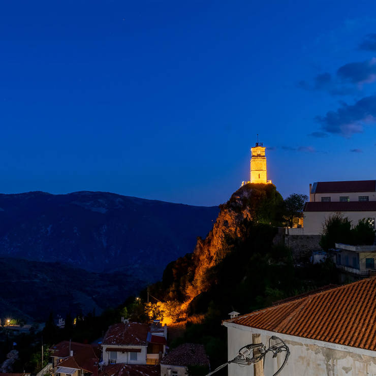 Illuminated clock tower of Arachova glowing at night against the dark mountain backdrop