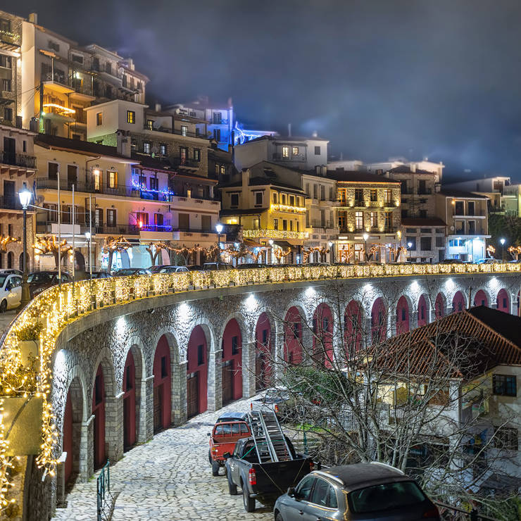 Night view of Arachova town center with festive lights and stone arches glowing under the mist