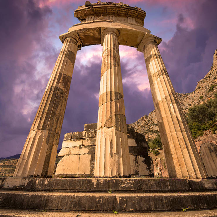 Ancient Tholos of Delphi with marble columns under a dramatic purple sunset sky