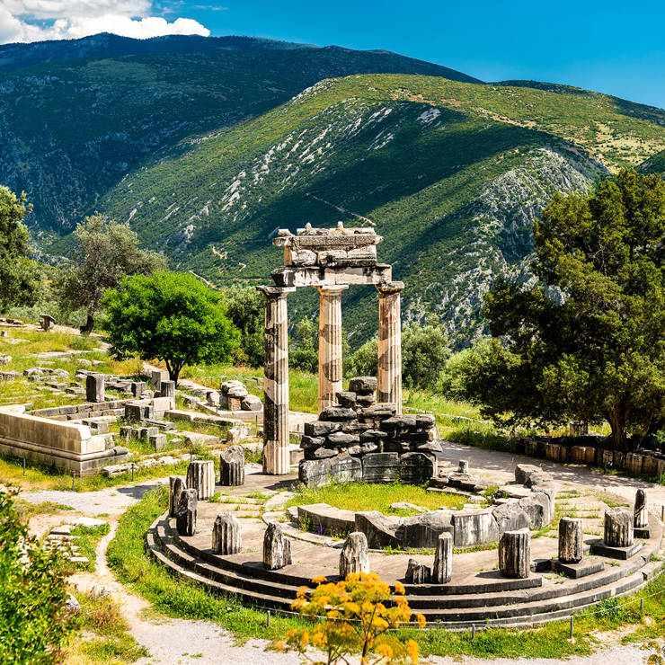 Marble columns of the Tholos of Delphi surrounded by ancient ruins and greenery
