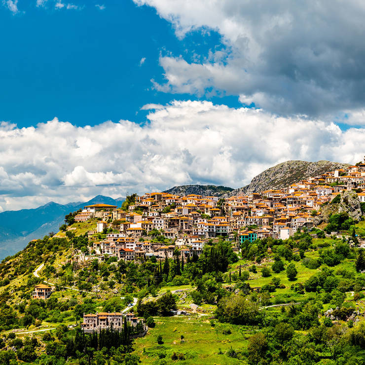 Scenic view of Arachova village built on the mountain slope with stone houses, green hills, and blue sky